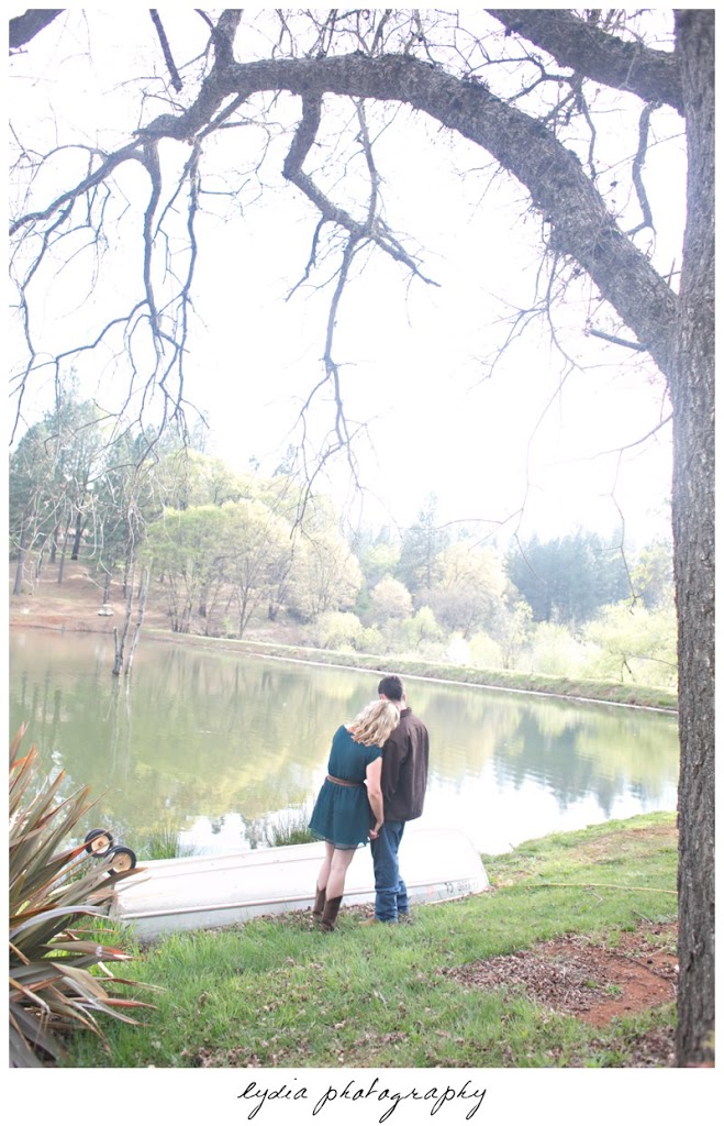 Bride and groom standing under a tree at lifestyle engagement portraits at a lake in Grass Valley, California