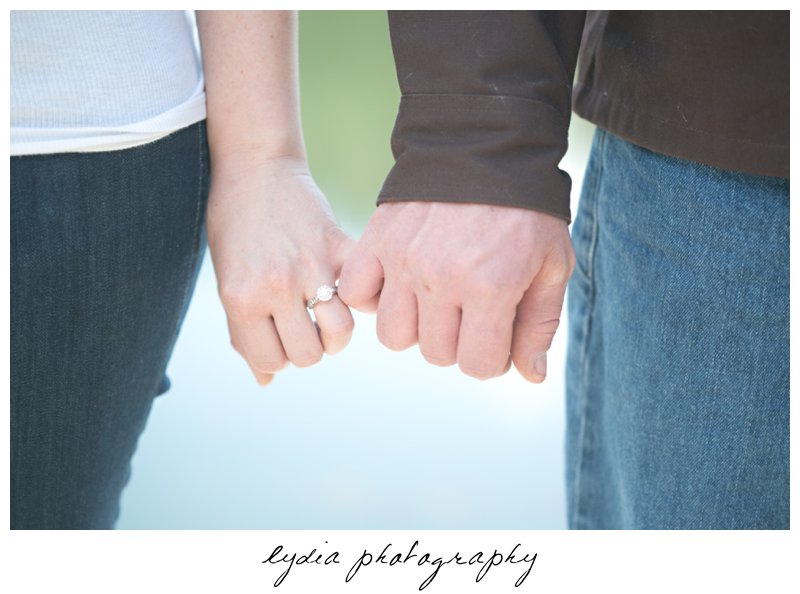 Bride and groom holding pinkies showing engagement ring at lifestyle engagement portraits at a lake in Grass Valley, California