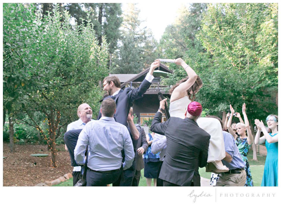 Bride and groom lifted up in chairs for Jewish horah dance at Harmony Ridge Lodge wedding in the Tahoe National Forest in California.