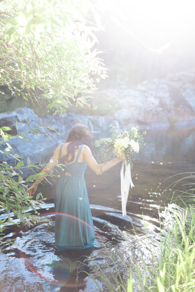 Bride holding up bridal bouquet and walking into water at Lake Wildwood wedding in Penny Valley, California