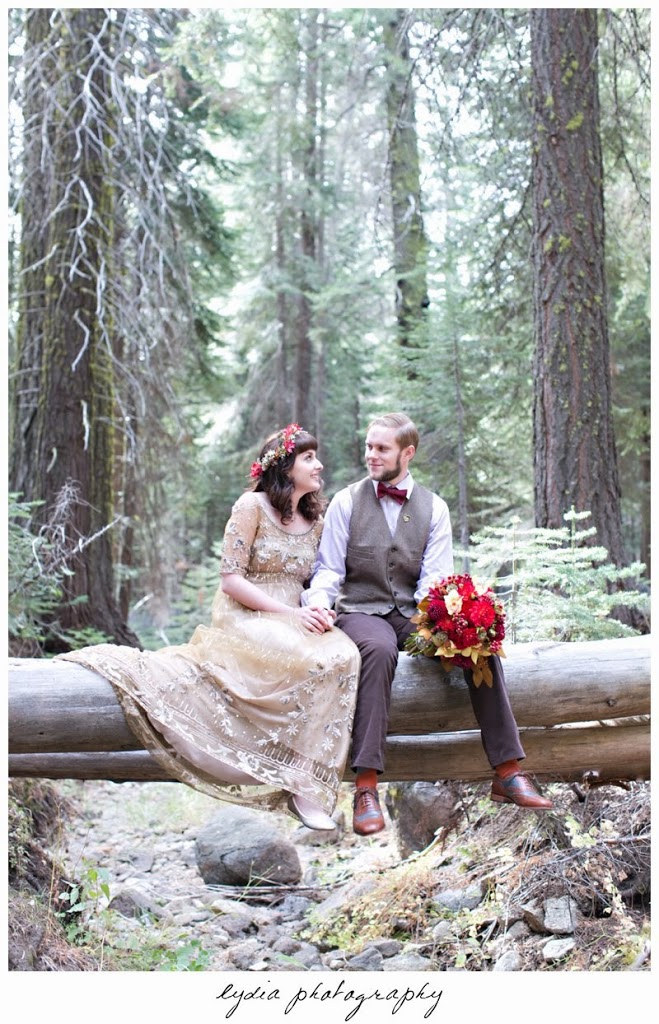Bride wearing Anthropologie gold dress and groom sitting on a log at intimate rustic vintage woodland wedding in Tahoe, California