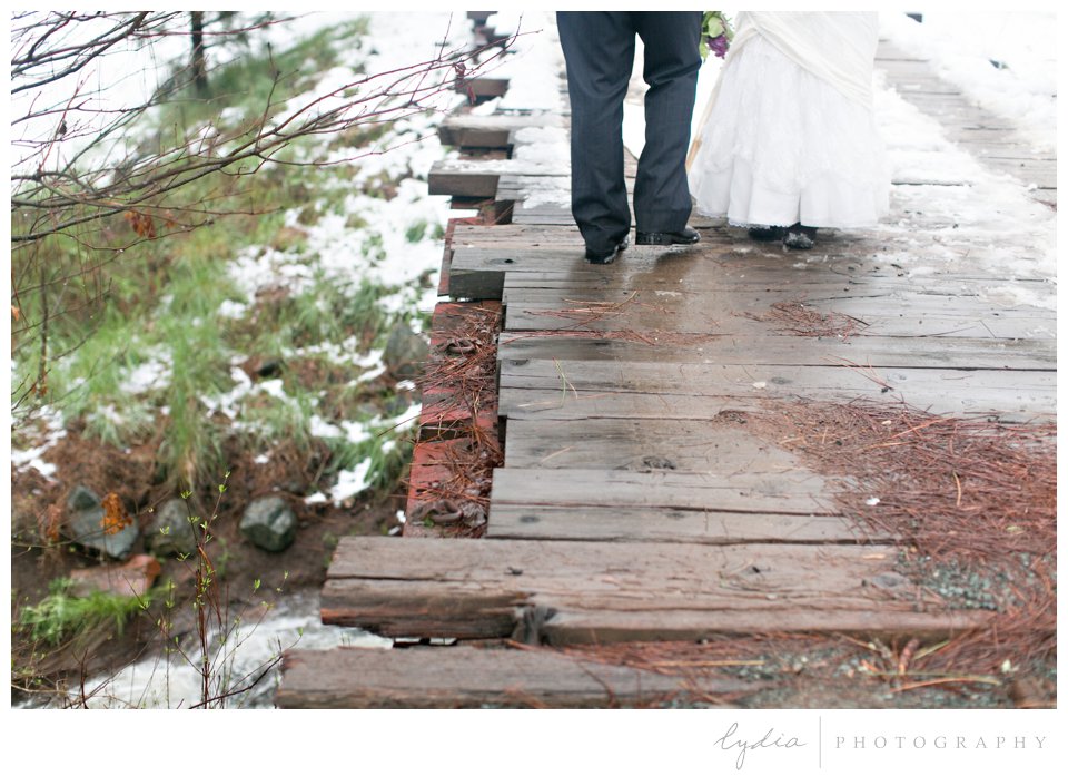 bride and groom walking over a snowy bridge