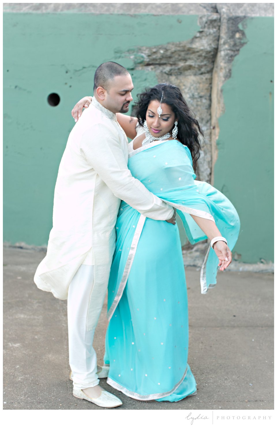 Indian bride wearing turquoise sari and silver bindi with groom with wind blowing on the cliff at Point Bonita
