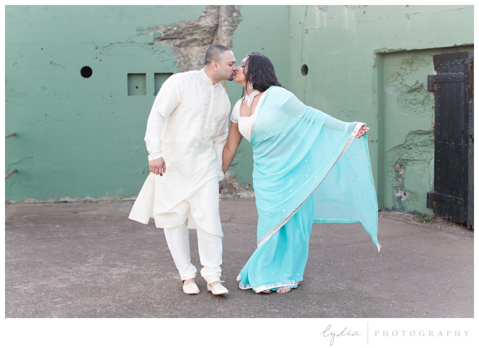 Indian bride wearing turquoise sari and silver bindi kissing groom