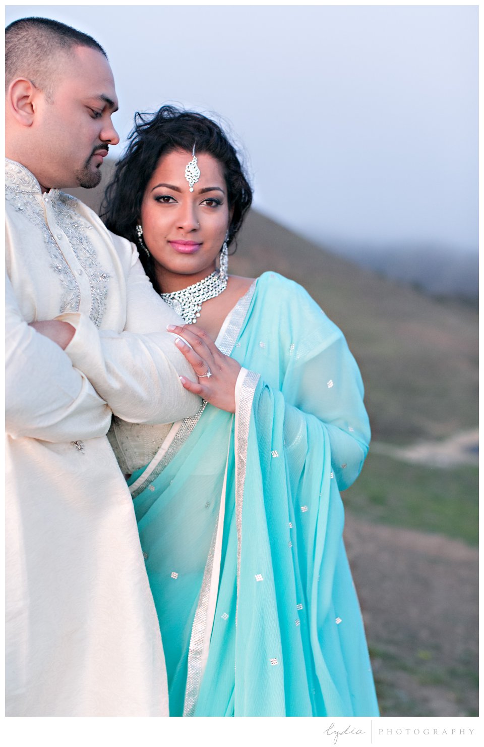 Indian bride wearing turquoise sari and silver bindi with groom on cliff at sunset at Rodeo Beach