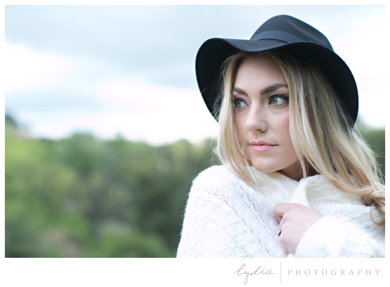 Anthropologie styled senior wearing a cozy sweater and black felt hat in a wildflower field in the rain in Roseville, California.
