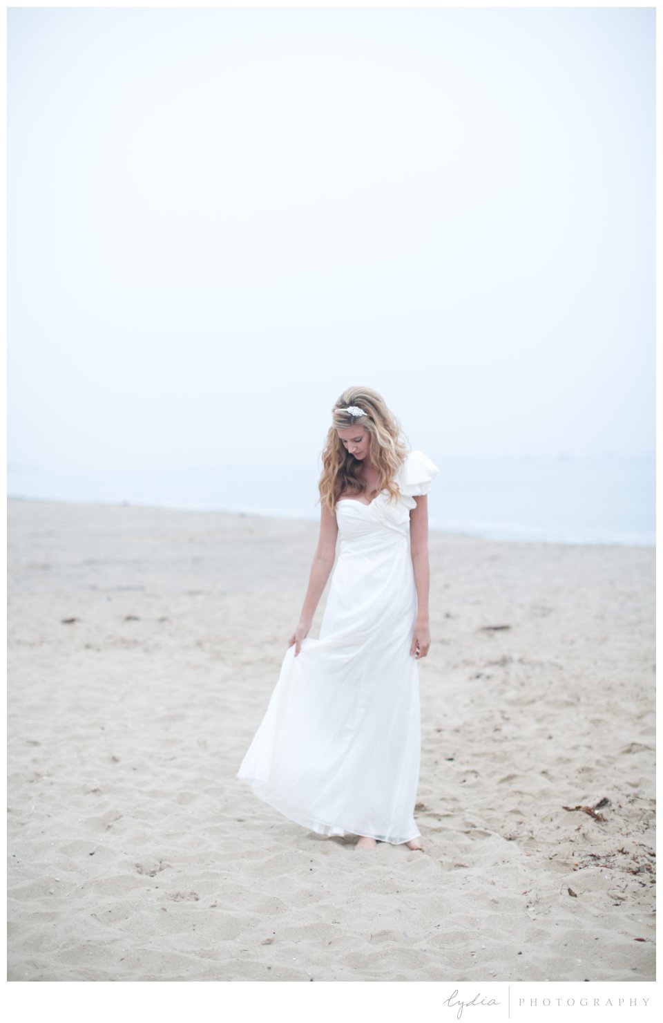 Bride holding up her wedding dress on ocean beach in Santa Barbara, California