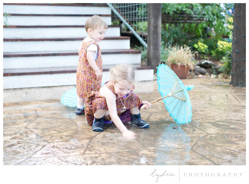 Children playing in the rain with parasol at rustic garden wedding in Chicago Park, California.