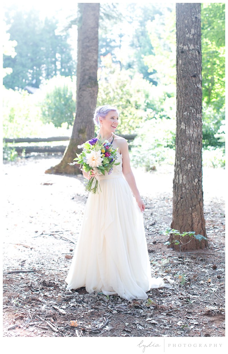 Bride with bouquet with sun rays on the trees at Harmony Ridge Lodge wedding in Grass Valley, California.