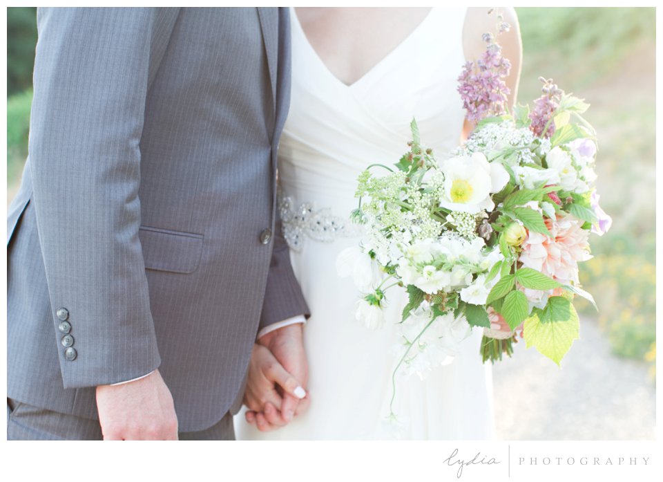 Bride and groom holding hands and bridal bouquet at Lucchesi Vineyards wedding in Grass Valley, California.