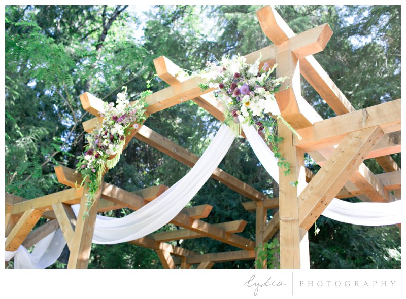 Wedding floral swags over arched pergola in the Tahoe forest at Harmony Ridge Lodge wedding in Nevada City, California.