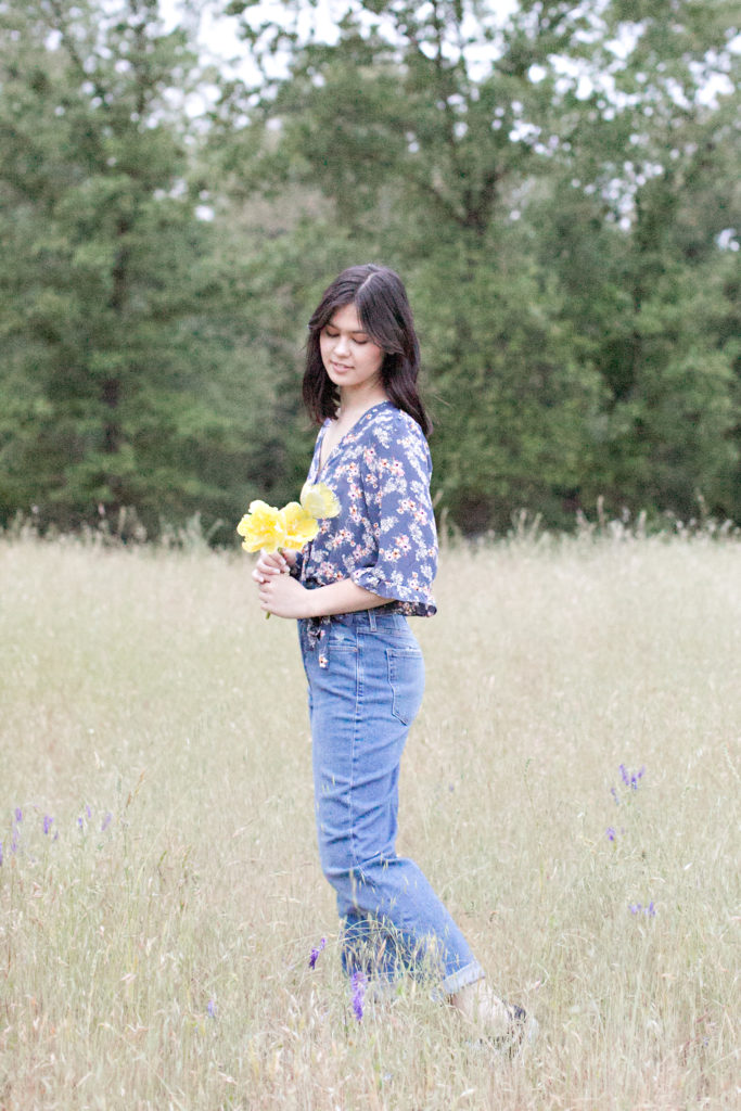 Teen girl standing in field holding flowers at Del Oro senior portraits