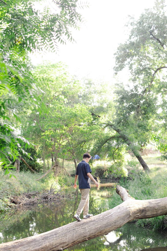 Young man standing on a log that spans a stream at a Roseville senior portrait session.
