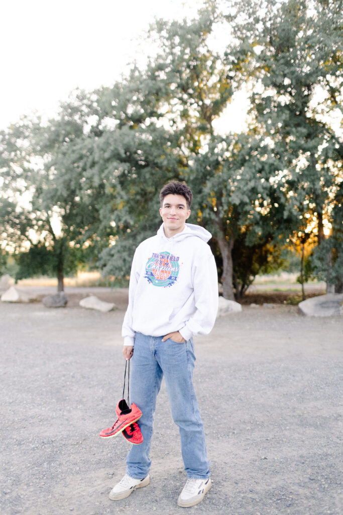 Young man holding running shoes at Roseville senior portrait session.